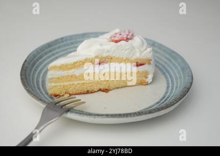 Una piccola shortcake giapponese alle fragole e una piccola forchetta su un elegante piatto giapponese su un tavolo bianco. Foto Stock
