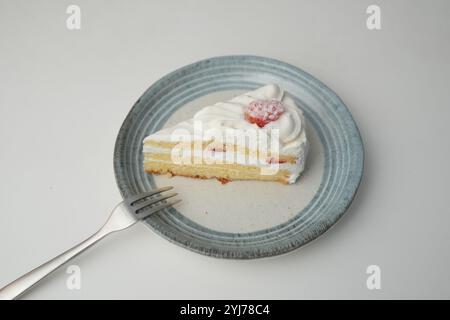 Una piccola shortcake giapponese alle fragole e una piccola forchetta su un elegante piatto giapponese su un tavolo bianco. Foto Stock