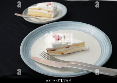 Piccola torta di fragole giapponese, forchetta e coltello ciascuno su due eleganti piatti grandi e piccoli in stile giapponese su un panno nero su un tavolo bianco. Foto Stock