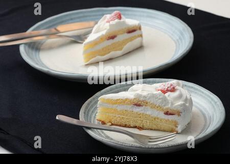 Piccola torta di fragole giapponese, forchetta e coltello ciascuno su due eleganti piatti grandi e piccoli in stile giapponese su un panno nero su un tavolo bianco. Foto Stock