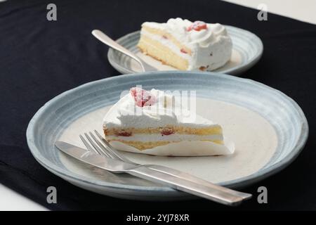 Piccola torta di fragole giapponese, forchetta e coltello ciascuno su due eleganti piatti grandi e piccoli in stile giapponese su un panno nero su un tavolo bianco. Foto Stock