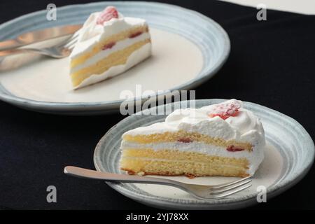 Piccola torta di fragole giapponese, forchetta e coltello ciascuno su due eleganti piatti grandi e piccoli in stile giapponese su un panno nero su un tavolo bianco. Foto Stock