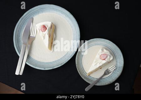 Piccola torta di fragole giapponese, forchetta e coltello ciascuno su due eleganti piatti grandi e piccoli in stile giapponese su un panno nero su un tavolo bianco. Foto Stock