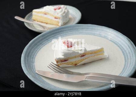 Piccola torta di fragole giapponese, forchetta e coltello ciascuno su due eleganti piatti grandi e piccoli in stile giapponese su un panno nero su un tavolo bianco. Foto Stock