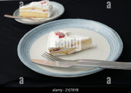 Piccola torta di fragole giapponese, forchetta e coltello ciascuno su due eleganti piatti grandi e piccoli in stile giapponese su un panno nero su un tavolo bianco. Foto Stock