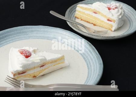 Piccola torta di fragole giapponese, forchetta e coltello ciascuno su due eleganti piatti grandi e piccoli in stile giapponese su un panno nero su un tavolo bianco. Foto Stock