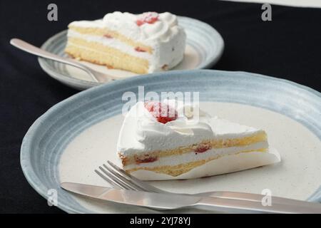 Piccola torta di fragole giapponese, forchetta e coltello ciascuno su due eleganti piatti grandi e piccoli in stile giapponese su un panno nero su un tavolo bianco. Foto Stock