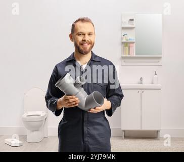 Idraulico in uniforme che tiene una pipa in bagno Foto Stock