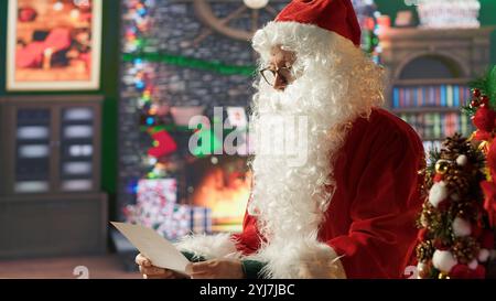 Il ritratto di Babbo Natale legge le lettere dei bambini e mostra un segno di silenzio, preparandosi per la consegna dei regali durante il suo viaggio nella stagione. Padre Natale porta i desideri alla vita, la magia delle vacanze. Telecamera A.. Foto Stock