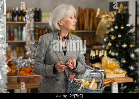 Donna anziana con cestino di alimentari in negozio Foto Stock