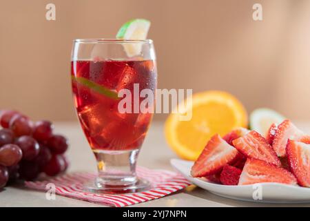 Primo piano di una tazza di bicchiere con vino estivo fatto in casa in primo piano accanto al piatto di fragole tritate su sfondo marrone chiaro Foto Stock