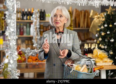 Donna anziana con cestino di alimentari in negozio Foto Stock