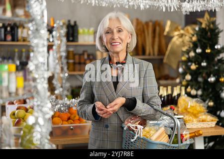 Donna anziana con cestino di alimentari in negozio Foto Stock