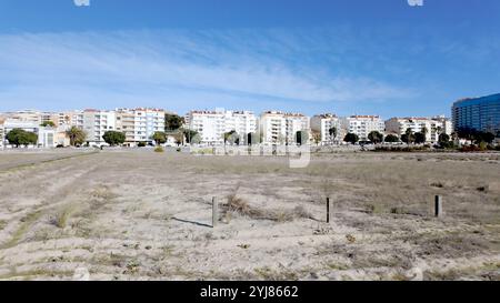 Una fila di appartamenti bianchi fiancheggia la costa e si affaccia su un vasto campo sabbioso sotto un cielo azzurro. Foto Stock