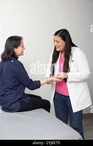 Latina medico donna assiste al paziente in ufficio esame riflesso parte dell'esame neurologico con il martello riflesso, colpisce il tendine Foto Stock