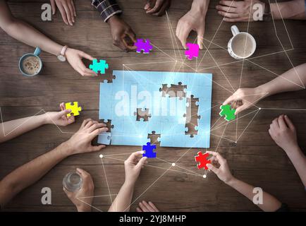 Persone che mettono insieme i pezzi del puzzle su un tavolo di legno, vista dall'alto. Schema per unirsi a loro. Concetto di partnership Foto Stock