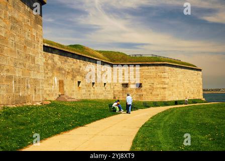 Le persone amano rilassarsi su una panchina del parco vicino alle imponenti mura della fortezza in pietra di Fort Independence a Boston Foto Stock