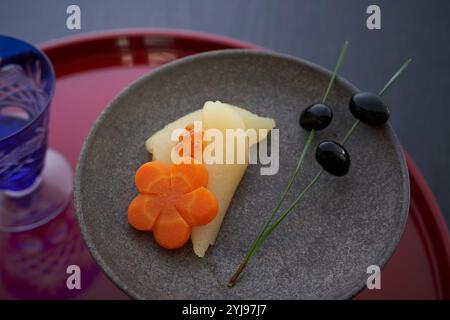 Vetro sfaccettato su un vassoio rotondo rosso e un piatto nero di soia nera con alcune uova di aringhe, carote e aghi di pino Foto Stock