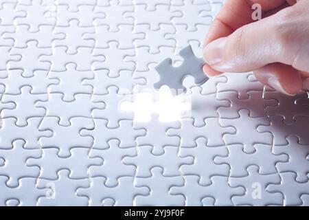 Mani con un puzzle bianco e un pezzo luminoso di puzzle bianco su un lato Foto Stock