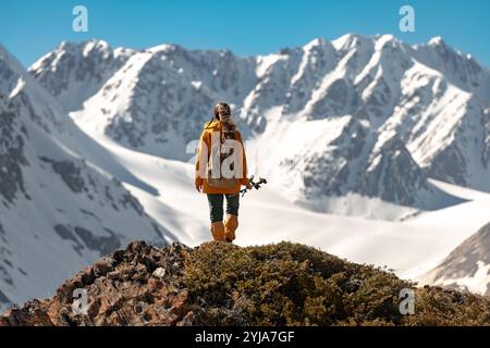 Una donna escursionista è in piedi con un piccolo zaino e bastoncini da trekking in cima alle montagne e guarda il ghiacciaio bianco Foto Stock