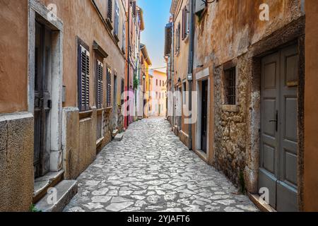 Rovigno, Croazia - strada stretta e vuota nella città vecchia di Rovigno in una soleggiata mattinata d'estate con tradizionali ciottoli, case colorate, finestre e. Foto Stock