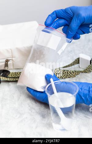 Mani con guanti per maneggiare la polvere di glucosio monoidrato in un sacchetto sigillato per un test di tolleranza al glucosio Foto Stock