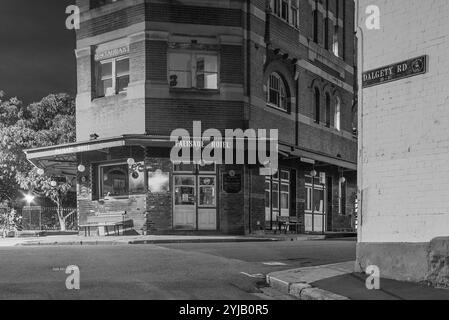 Il sobborgo The Rocks di Sydney, insediato durante la colonizzazione nel 1788, contiene molti monumenti storici ed è il più antico sobborgo dell'Australia. I suoi edifici, le scale e gli archi furono costruiti con arenaria locale, da cui il nome della zona. Fino agli anni '1870 era uno slum dove le "bande di rasoi" si riversavano di notte in vicoli. Oggi è un quartiere turistico ricco di storia circondato da Dawes Point, Millers Point e Barangaroo, spesso considerato parte del distretto di Rocks. Nella foto: Vista notturna del Palisade Hotel a Millers Point in The Rocks su Bettington Street a Dalgety Road. Foto Stock