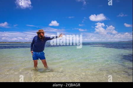 Un uomo si trova in acque poco profonde su una spiaggia a Mauritius, godendosi l'oceano. Foto Stock