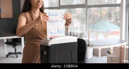 Giovane segretaria che distrugge i documenti usando il tritadocumenti in ufficio Foto Stock