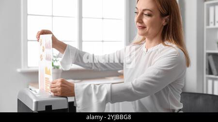 Segretaria matura che distrugge i documenti usando il tritadocumenti in ufficio Foto Stock