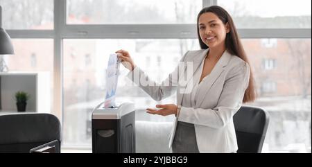 Giovane segretaria che distrugge i documenti usando il tritadocumenti in ufficio Foto Stock