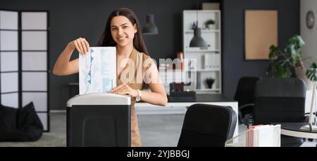 Giovane segretaria che distrugge i documenti usando il tritadocumenti in ufficio Foto Stock