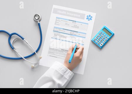 Medico mano che riempie il modulo di assicurazione sanitaria vicino allo stetoscopio e calcolatrice su sfondo bianco Foto Stock