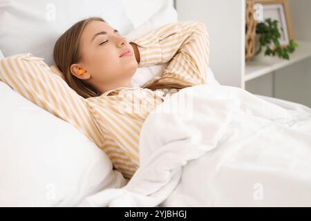 Giovane donna con tappi per le orecchie che dorme in camera da letto Foto Stock