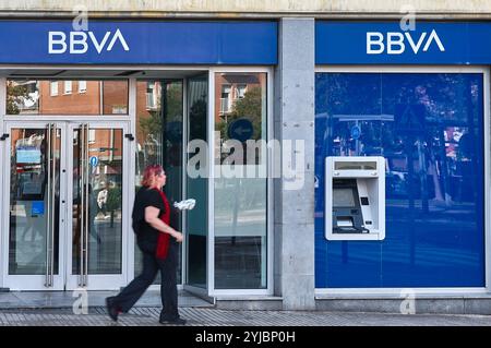 Viladecans. Spagna - 14 novembre 2024: Questa immagine cattura l'esterno di una filiale di banca BBVA, con una donna che cammina oltre l'ingresso. Gli archi moderni Foto Stock