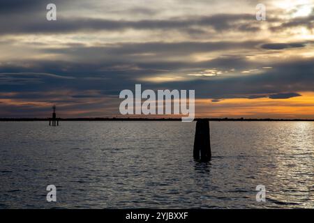 Un tranquillo tramonto rosso sulla laguna, con i mattoni veneziani (limite del canale navigabile) retroilluminati sul mare, Chioggia, Venezia, Italia Foto Stock