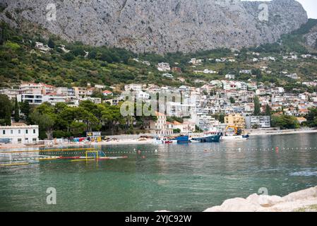 Lungomare di Omis con vista sulla città e sulle montagne, Croazia. La splendida costa si fonde con l'aspro sfondo delle montagne, creando un paesaggio pittoresco Foto Stock