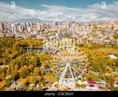 Erevan, Armenia - 19 ottobre 2024: Vista panoramica aerea della ruota panoramica nel Parco della Vittoria con paesaggio urbano ed edifici di Erevan. Soleggiata giornata autunnale ca Foto Stock