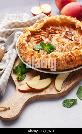 galette di mele appena sfornata decorata con scaglie di mandorle e menta, servita su un tavolo con mele fresche e un coltello Foto Stock