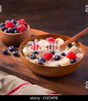 Sana avena tagliata in acciaio con banana, mirtilli, lamponi e latte di mandorle in un recipiente marrone Foto Stock