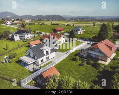 Vista aerea, drone che sorvola la comunità suburbana in campagna. Case di famiglia nei sobborghi circondate da boschi e campi verdi Foto Stock