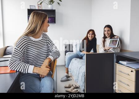 Gruppo di tre coinquiline, studentesse universitarie, giovani donne caucasiche, che trascorrono del tempo insieme nella loro stanza, studiano, parlano, si divertono, ridono Foto Stock