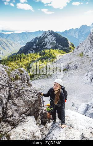 Alpinista caucasica che sale la montagna su via ferrata, in cima alle cime. Donna che indossa un copricapo protettivo e l'uso Foto Stock