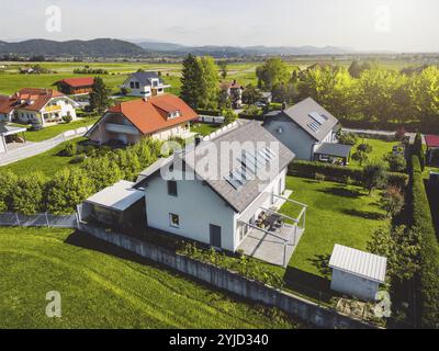 Vista aerea, drone che sorvola la comunità suburbana in campagna. Case di famiglia nei sobborghi circondate da boschi e campi verdi Foto Stock