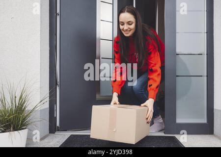 Giovane donna allegra eccitata per un pacco che ha appena ricevuto. Donna che riceve il suo regalo di natale per posta. Aprendo il regalo di Natale a casa Foto Stock