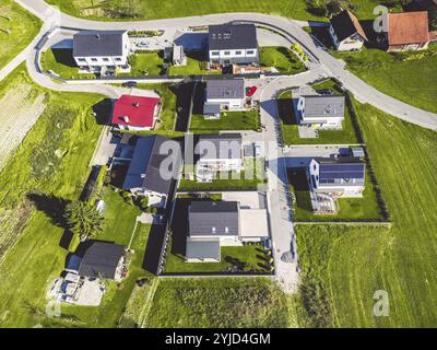 Vista aerea, drone che sorvola la comunità suburbana in campagna. Case di famiglia nei sobborghi circondate da boschi e campi verdi Foto Stock