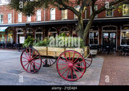 Savannah, Georgia, USA - 20 febbraio 2024: Un carro colorato traboccante di piante si trova vicino a una vivace area ristorante, che esalta il fascino locale. Foto Stock