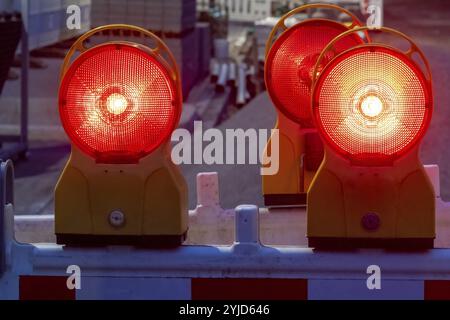 Le spie rosse lampeggiano su una barriera da cantiere al crepuscolo, segnalando attenzione e garantendo la sicurezza Foto Stock