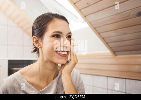 Bella giovane donna che pulisce il viso, rimuovendo il trucco con un panno di cotone e acqua micellare. Cura e bellezza della pelle. Giovane bella donna che pulisce h Foto Stock