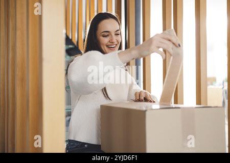 Giovane donna allegra eccitata per un pacco che ha appena ricevuto. Donna che riceve il suo regalo di natale per posta. Aprendo il regalo di Natale a casa Foto Stock